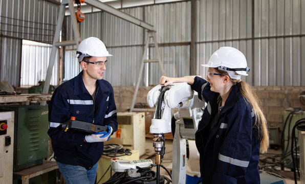 Engineers collaborate on robotic arm project in industrial workshop during daytime