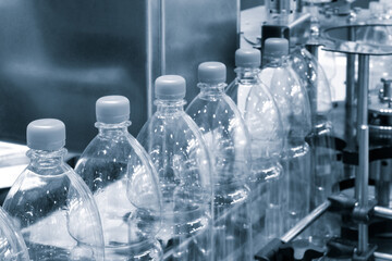 Bottles of water are being filled at a factory. The bottles are clear and have a plastic cap