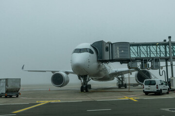 Low angle view of an airplane parked at a gate at an airport terminal on a gloomy foggy day