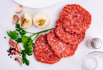 Shaped patties for burgers from raw ground beef meat with fresh parsley sprigs, spicy garlic and allspice on white table