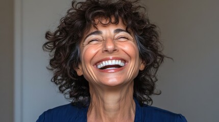A woman with curly hair beams with happiness in a well-lit indoor location. Her genuine smile and joyful expression convey warmth and positivity, embodying a moment of pure delight