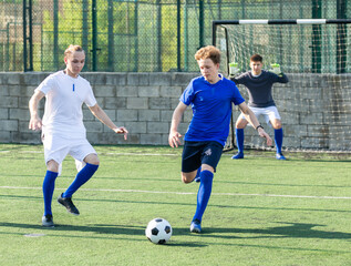 Obraz premium Game moments of football match between two teams of teenagers in white and blue shirts