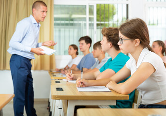 Pupils sitting in class and listening carefully to male teacher.