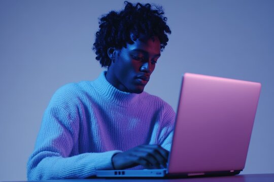 Young man using laptop under vibrant blue and purple lighting.
