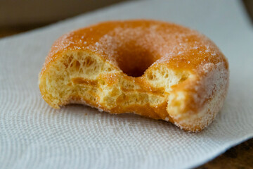 A fresh sugar topped donut from the bakery sitting on a white paper napkin with bite marks in it after being eaten.