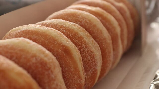 A dozen fresh donuts from the bakery topped with sugar laying inside of a cardboard box.