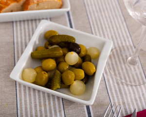 Plate with delicious pickled olives, gherkins and baby onions on dining table. Popular Spanish snack