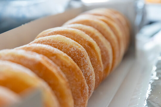 A dozen fresh donuts from the bakery topped with sugar laying inside of a cardboard box.