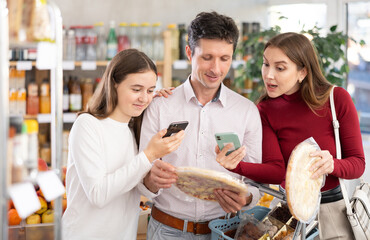 Attentive teen girl with her parents checking barcode on half-finished pizza in supermarket