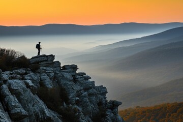 Obraz premium A lone hiker pauses on a rocky outcrop, gazing at a breathtaking sunset over layered mountains.