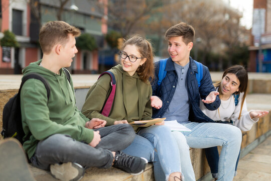 Smiling cheerful teenagers talking with each other sitting on stairs on city street