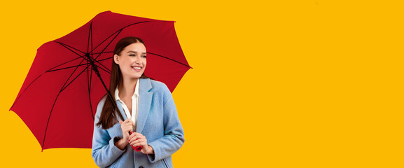 Cheerful stylish lady in coat standing with umbrella and looking aside at free space for your advertisement or text