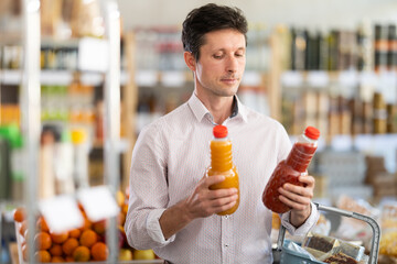 Man choose and buy fruit juice in store. Visitor make choice of assortment, buy fresh juice. Customer read label, examine packaging and choose drink