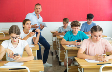 Pupils sitting in class room and watching in their smartphones.