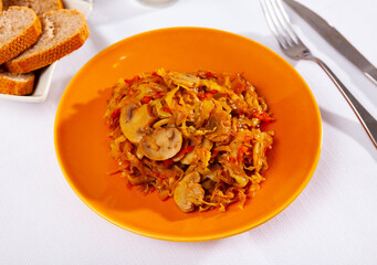 Portion of stewed white cabbage with mushrooms champignon is piled on plate. Delicious and healthy dish of national German cuisine