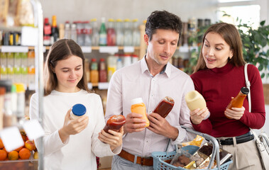 Positive family with teenage girl choosing the best sauce in grocery store