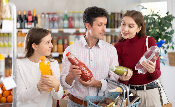 Positive family with teenage girl choosing various non-alcoholic drinks in grocery store