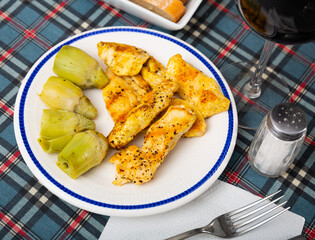 Grilled chicken fillet with artichokes on a ceramic plate, served with wine