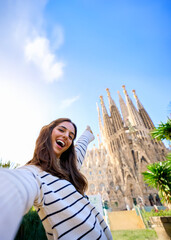 Vertical. Young funny caucasian women taking a selfie in front of Sagrada Familia in Barcelona. Smiling beautiful girl on European street city enjoying vacation happy and smiling. Funny tourism people