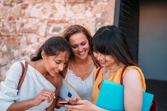University exchange students using smartphone near brick wall