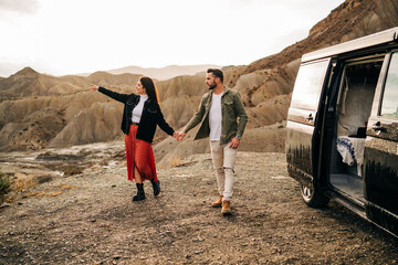 Young couple holding hands and exploring the desert landscape near their camper van
