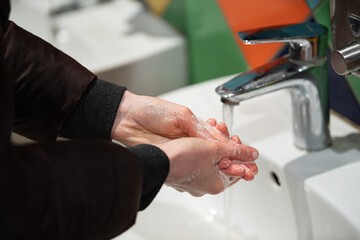 Hands covered with soap are being washed under flowing water at a public sink, highlighting the importance of cleanliness and promoting hygiene practices among users