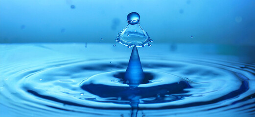 Blue drop of water falling on the surface, a spray of small drops around_