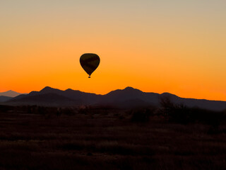 Single hot air balloon flying low over hills in the desert of Phoenix Arizona during beautiful sunset