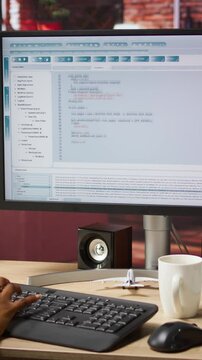 Vertical video Woman in home office looking at UI on PC screen, typing and executing programming code. Coding application UI used by IT developer writing and testing code in modern apartment, camera A