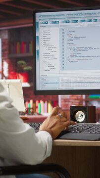 Vertical video Programmer wearing headphones types code into PC, developing software programs, entering commands. Woman at home fixing errors in application, implementing new features, listening music