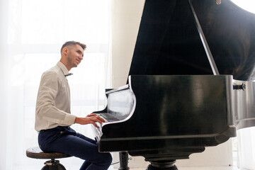 young guy in white shirt plays on old black piano, musician pianist performs melody on acoustic...
