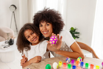 African American mother and daughter celebrate Easter and paint eggs with farbe and brush at home,...