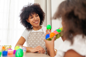African American mother and daughter celebrate Easter and paint eggs with farbe and brush at home,...