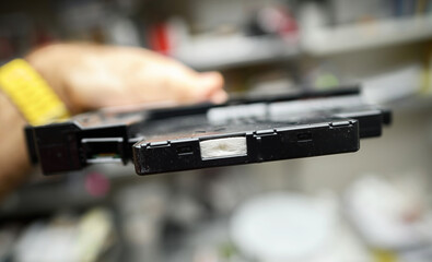 Close-up of a printer part held in hand, showing intricate details of the black plastic casing and an internal compartment in a workshop background.