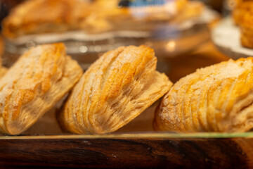 A tray of golden-baked pastries in a glass display case for sale. The decadent buttery buns are...