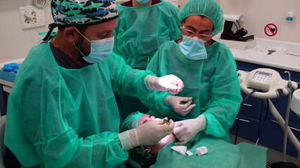 Team of dentists sewing up the mouth of an anesthetized patient