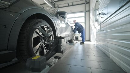 Mechanic performing a wheel alignment process in a modern workshop. Professional equipment is used to ensure accurate vehicle alignment for optimal performance and safety