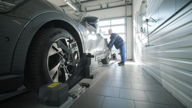 Mechanic performing a wheel alignment process in a modern workshop. Professional equipment is used to ensure accurate vehicle alignment for optimal performance and safety