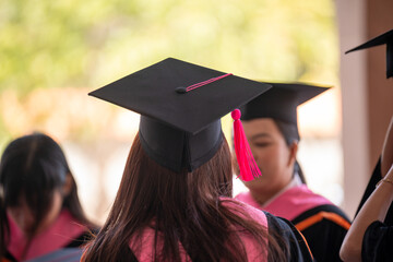 A woman wearing a black cap and gown is standing in front of other graduates. Concept of accomplishment and pride as the graduates celebrate their achievements