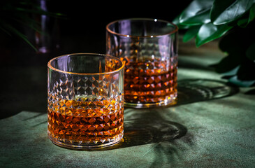 Japanese whiskey single malt in rocks glass. Dark green background with tropical leaves