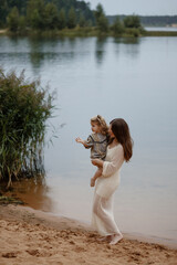 A woman in a white dress carries a child at a tranquil lakeside, surrounded by nature's beauty, evoking a sense of peacefulness, serenity, and family bonds.