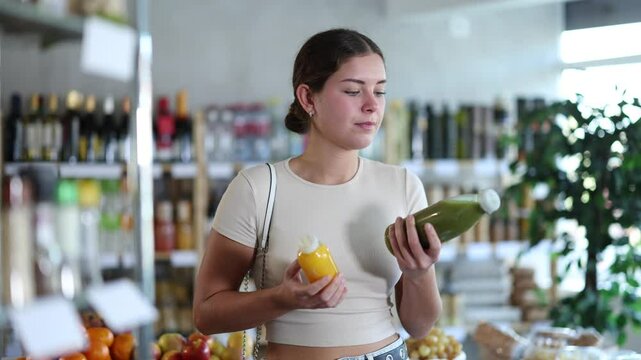 Young woman buyer chooses fresh smoothies in bottle in grocery store 