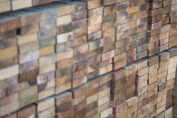Stacked wooden planks in a lumberyard, showing various shades and textures of the wood, arranged in neat rows..