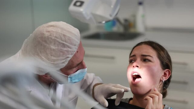 Girl is sitting in armchair during dental diagnosis at dentist appointment. Senior man doctor conducts examination procedure, identifies problem areas and tests sensitivity of teeth