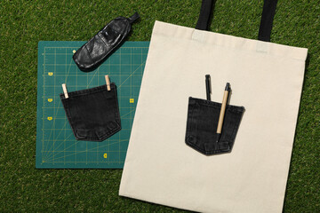 Drawing, cotton bag and denim pockets on green background, top view