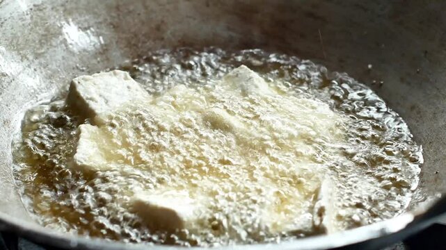 4k video of frying tofu in a pan filled with cooking oil.