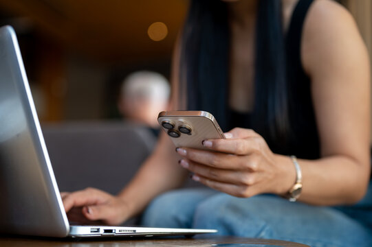 A close-up of a woman holding her smartphone while working on her laptop.