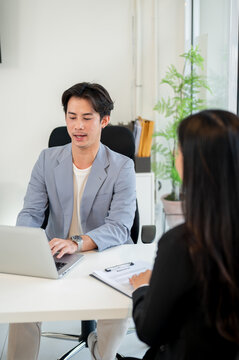 A professional Asian businessman is working on his laptop while interviewing a candidate in office.
