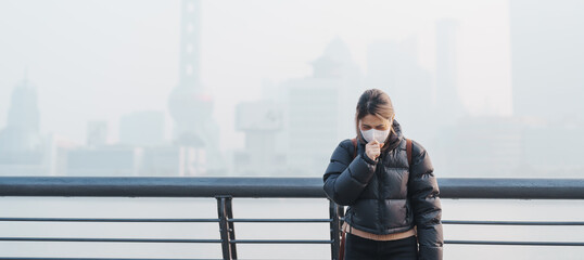 young Asian woman wearing respiratory mask protect and filter pm or particulate matter against bad Air Pollution in Shanghai City, China. Air Quality Index, AQI, Unhealthy, healthcare concept © Jo Panuwat D