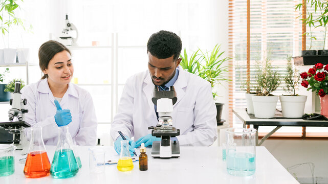 Two scientists collaborate in a bright lab, using a microscope and various colorful liquids for their research. Group of chemistry students working in the laboratory with the microscope and chemical.
